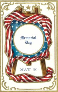 antique post card of a plaque on an easel. The plaque is round and centered in the middle in black lettering are the words Memorial Day. It is set in a square frame of blue and white stars. The entire thing is surrounded by red and white striped bunting.