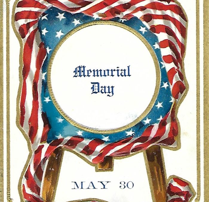 antique post card of a plaque on an easel. The plaque is round and centered in the middle in black lettering are the words Memorial Day. It is set in a square frame of blue and white stars. The entire thing is surrounded by red and white striped bunting.