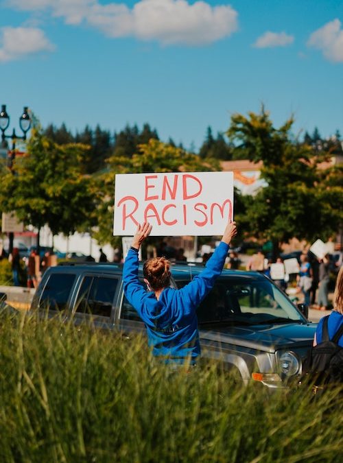 woman holding a sign that reads "End Racism" at a rally
